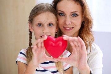 Beautiful smiling woman and kid hold red toy heart