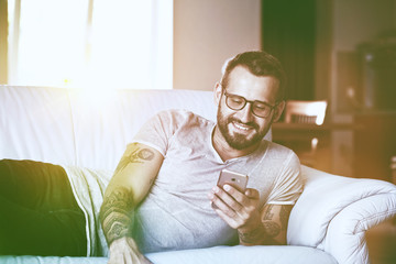 smiling man with smart phone lying on couch