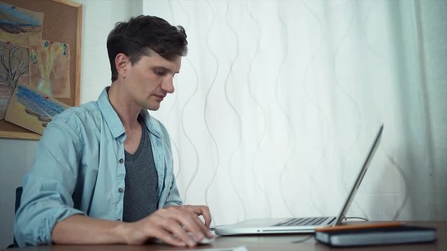 Young handsome man uses laptop makes notes in documents. Freelancer working home