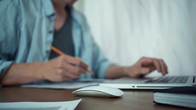 Male hands using wireless mouse making note with pencil at analyzing graphs