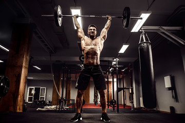 Muscular fitness man doing deadlift a barbell over his head in modern fitness center. Functional...