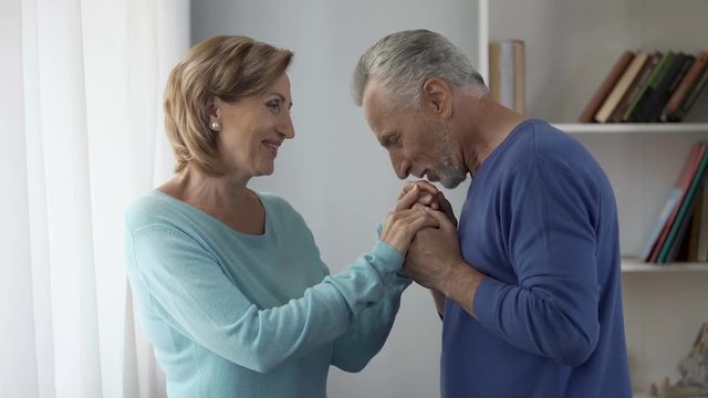 Aged man holding woman hands, kissing them in turns, lady being shy, coquette