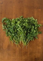 Bunch of fresh, wet garden parsley stems with little imperfections on wooden background