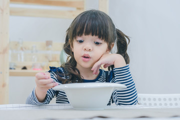 A little cute girl having a breakfast in the dinning room, eating cereal and milk in white bowl, healthy food