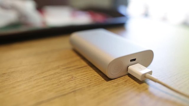 Powerbank external battery charging smartphone or tablet pc lying on the table. The indicator flashes. Close up shot.