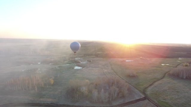Hot air balloon is flying at sunrise, aerial view. Footage. White Hot Air Balloon in the Sunrise Sky - Powered by Adobe