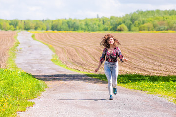 Fototapeta na wymiar Young woman running on countryside road by brown plowed fields with furrows in summer in Ile D'Orleans, Quebec, Canada