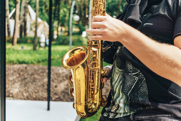 Obraz premium Street musician saxophonist plays jazz music in park in sunny day