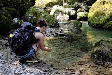 female hiker drinks from clear mountain stream