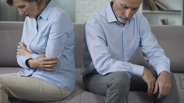 Aged couple sitting on couch turned away from each other, relationship crisis