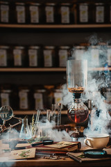 Brewing coffee in vacuum coffee maker with rising steam and a floral still life. Alternative coffee brewing method. Botanist workplace.