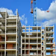 Construction site. Unfinished high raised building with big industrial tower crane and blue sky in background. Modern civil engineering. Contemporary urban landscape.