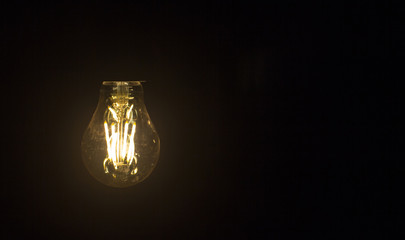 Light bulb hanging on black background. Copy space