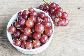 Red grape fruit in white bowl on wooden table. Copy space.