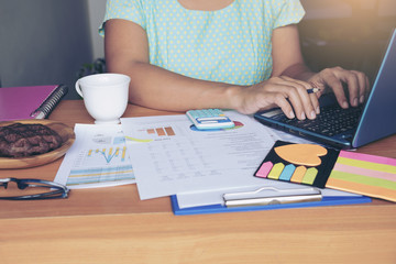 Top view of young working woman using laptop and reading report , graphs , charts, document at work. Business woman working at her desk.