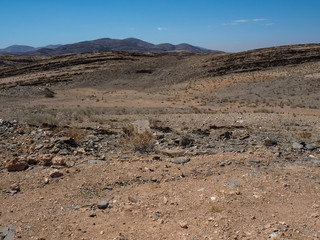 Rock mountain dried dusty landscape ground of Namib desert with splitting shale, other stone and desert plant