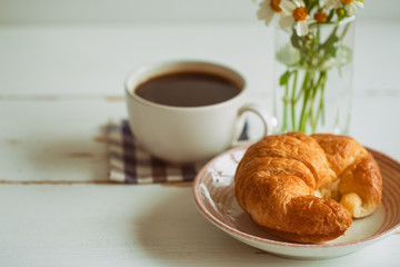 Homemade croissant on plate served with black coffee or americano. Delicious and quick breakfast with fresh croissant and coffee. Croissant and black coffee for breakfast on wood table with copy space