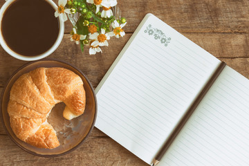 Homemade croissant served with black coffee or americano. Delicious breakfast with fresh croissant and coffee. Croissant and black coffee with open notebook and pencil in top view or flat lay style.