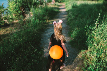Portrait of child girl with blonde hair and blue eyes, she has fun with ballon  in the forest