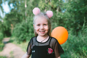 Portrait of child girl with blonde hair and blue eyes, she has fun with ballon in the forest