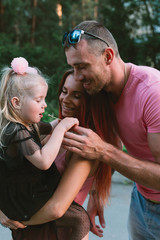 Young family portrait, mother, father and daughter having fun together and hug each other. They blow on a dandelion