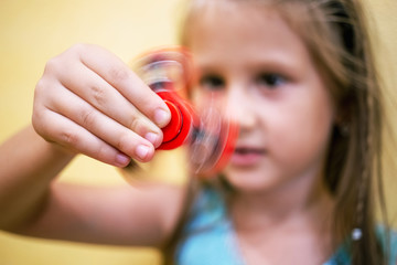 Little girl playing with red fidget spinner toy to relieve stress at home