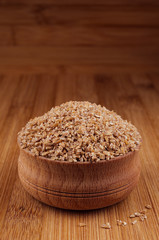 Wheat groats in wooden bowl on brown bamboo board, closeup. Rustic style, healthy dietary cereals  background.