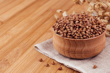 Buckwheat brown in wooden bowl on brown bamboo board, closeup. Rustic style, healthy dietary groats  background.
