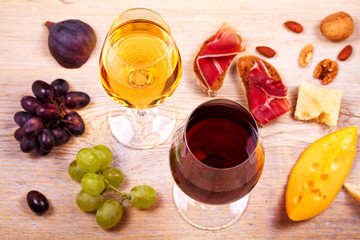 Glasses of red and white wine with cheese, prosciutto, figs and grape. Wineglass on wooden table. Wine still life. Food and drinks concept. View from above, top studio shot, horizontal