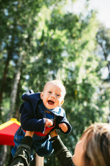 Mother hands tossing up the high air joyful baby boy. Outdoors healthy child activity, active lifestyle and having fun on family summer vacation with son at the playground.