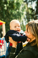Portrait of mother who hug her joyful baby boy. Outdoors healthy child activity, active lifestyle and having fun on family summer vacation with son at the playground.