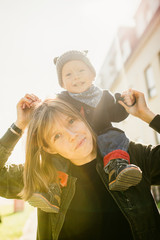 Happy young mother with her son on her shoulder, enjoying the sunshine, they smile and laugh.Outdoors healthy child activity, active lifestyle and having fun on family summer vacation with son at the 
