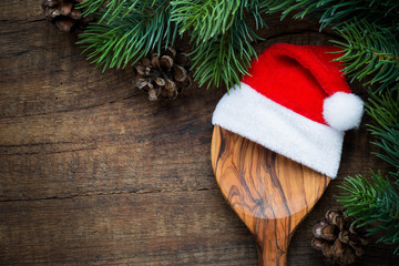 Christmas cooking concept - A wooden spoon with Santa hat and pine cones on dark rustic wooden...