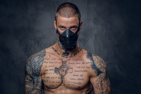 Shirtless, tattooed male in a mask over grey background.