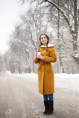 Beautiful young girl walking in winter in a snow-capped city with cup of hot coffee