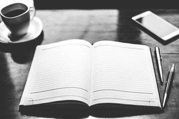 Black and white photo. Notebook with pens and phone on the wood table