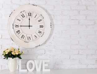 wooden letters forming word LOVE, flowers and vintage clock over white brick wall
