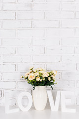 rose flowers and wooden word love over white brick wall