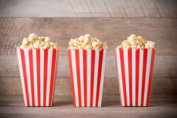 Popcorn in red and white cardboard on wooden table.