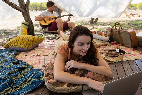Woman using laptop with man playing guitar in tent