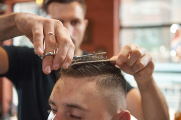 Close up shot of a barber using scissors cutting hair of his male customer. 