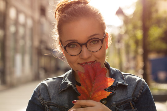 Beautiful woman holding autumn leaf on the street. Autumn concept.