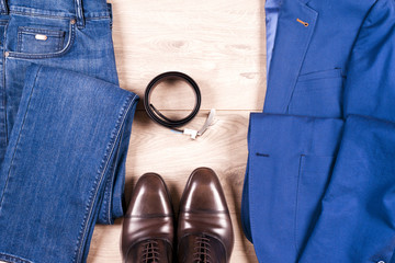 set of classic mens clothes - blue suit, shirts, brown shoes, belt and tie on wooden background.