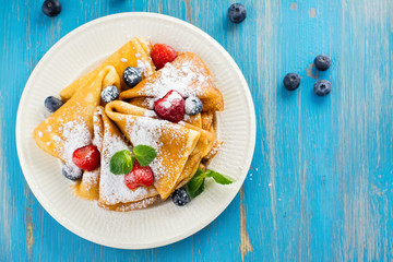 Crepes with jam, berries and sugar powder. Homemade pancakes, delicious breakfast