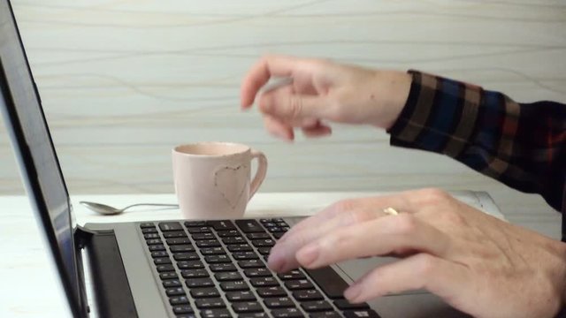 girl typing on a laptop keyboard and drinking a coffee
