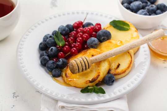 Cottage cheese pancakes syrniki with berries and honey on white background. Space for text