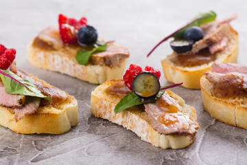 Bruschetta sandwiches with duck meat, fig sauce and berries on stone table. Space for text