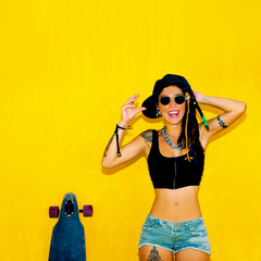 Cool Happy girl with dreadlocks, piercings and longboard over colorful yellow wall