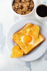 Breakfast for Valentines day: toast with heart shaped egg, muesli and coffee on white concrete table. Space for text