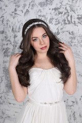 Fototapeta premium Pretty young brunette in diadem and with hairdo poses in white studio